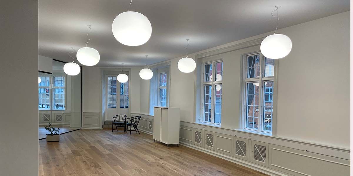 En tom kontor med hvide vægge og loft, højt til loftet, store runde loftslampe, trægulv, møbler og planter