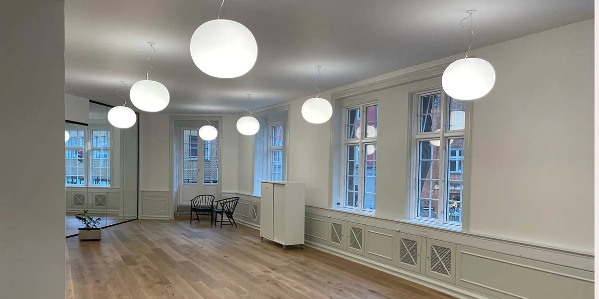 En tom kontor med hvide vægge og loft, højt til loftet, store runde loftslampe, trægulv, møbler og planter