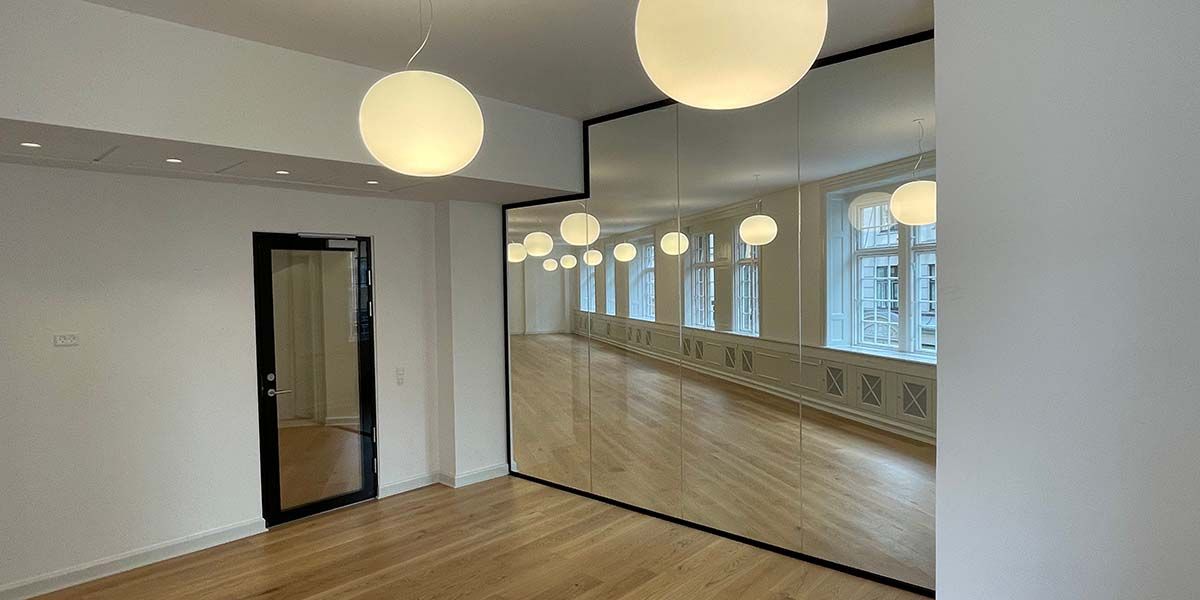 Et stort, tomt kontor med lyse loftslampe og spejl. Gulvet er lavet af træ og gulvet er renset. Der er en dør i højre