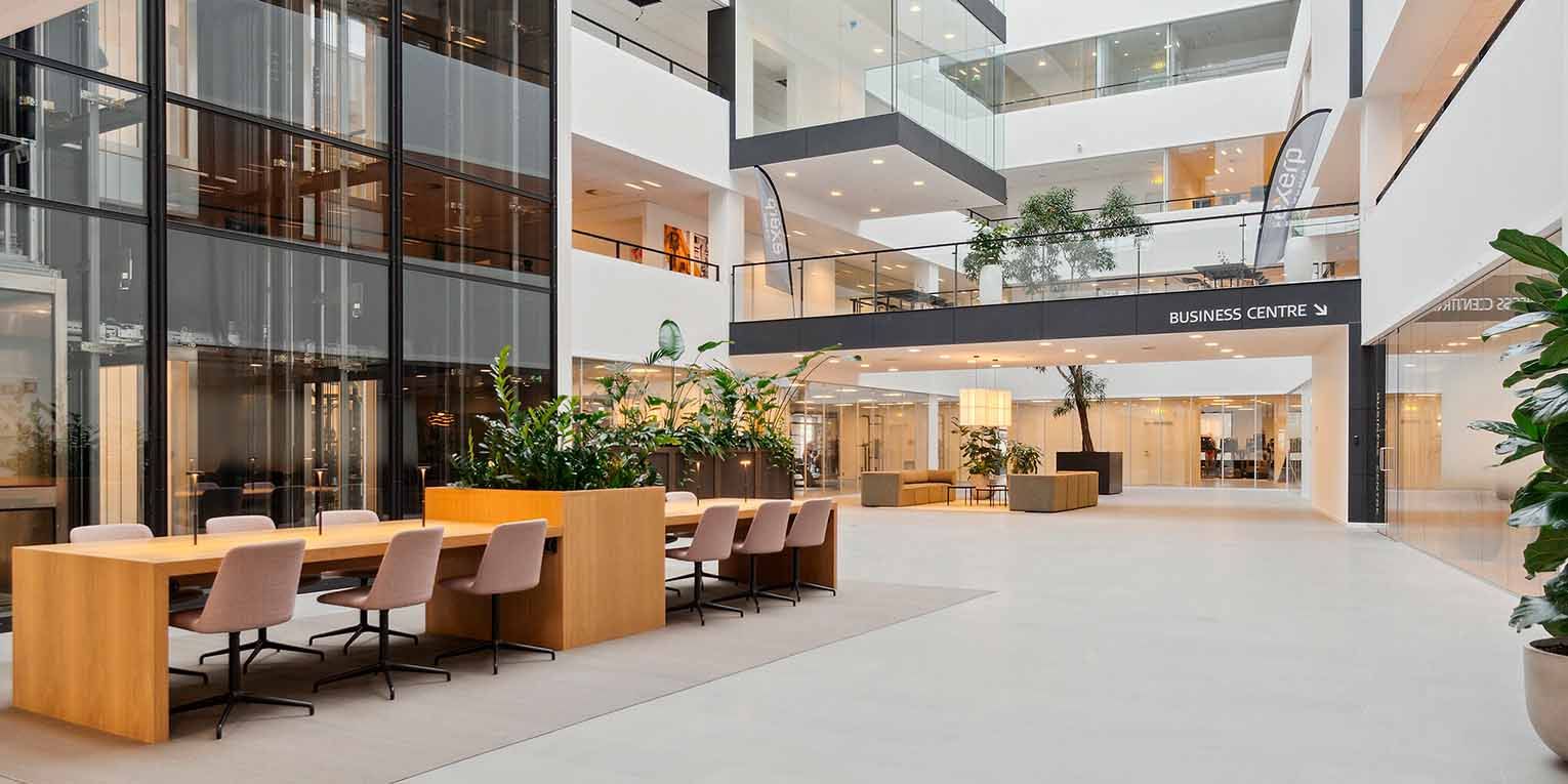 Moderne kontor i Mikado House med bord og stole, store vinduer og indvendige planter og træer