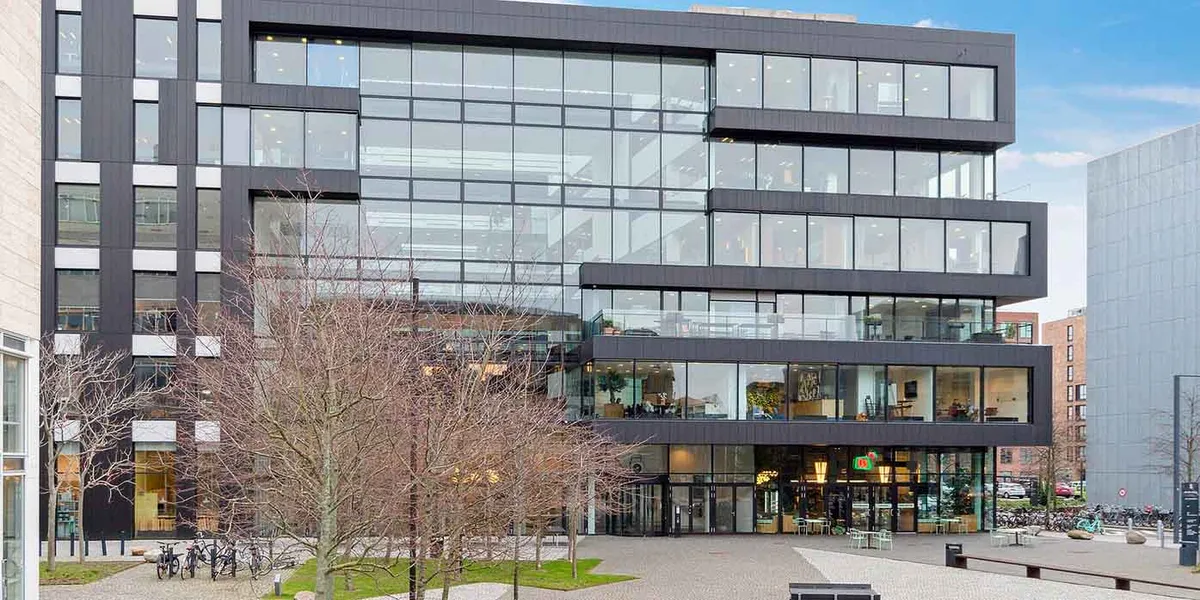 Et stort moderne bygning med glasvinduer og plantetræer foran. Væggene er lige og der er flere terrasser.