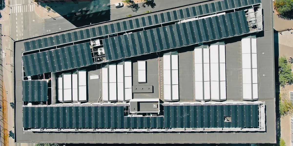 Et stort bygning med solceller på taget og flere hvide vægge med højde. Solcellerne er arrangeret i rækker og dækker store
