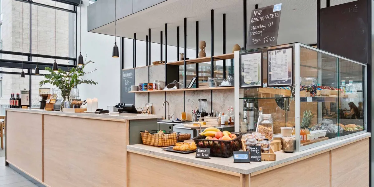 Buffet med frugt, brød, chokolade og juice i et moderne cafémiljø med store vinduer og højt til loftet