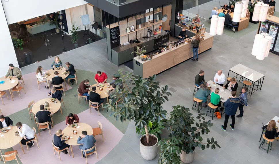 Moderne og stilfuldt indrettet flerbrugerhus med flere mennesker, der spiser på lange runde borde og søjler med store