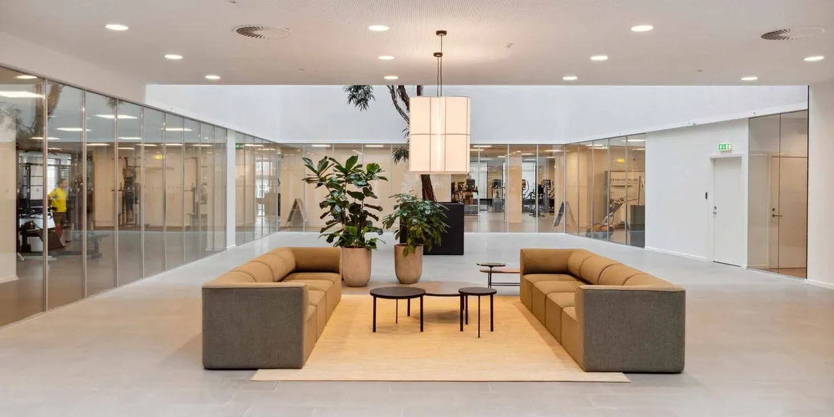 Moderne lobby med to komfortable sofaer, tre kaffeborde og et stort lysekron. Væggene er fuldstændig glas, og der er