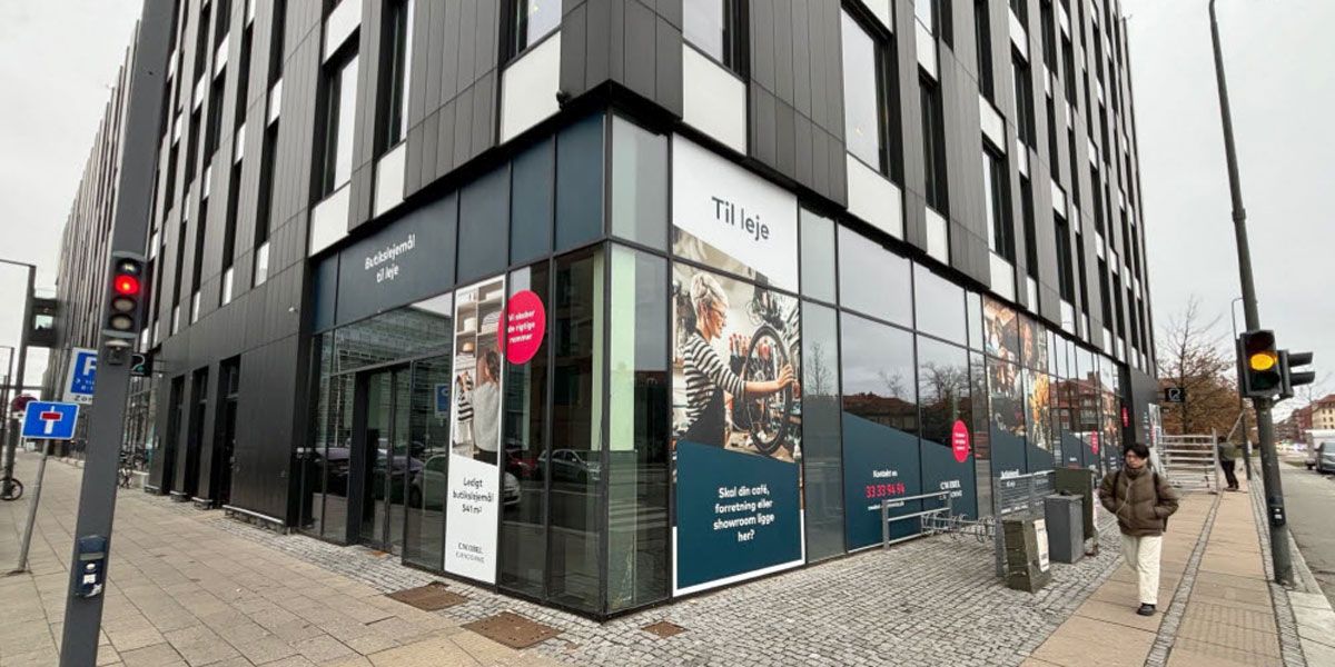En mand går forbi en butiksfront med skiltet Til leje. Butikken har glasvinduer og vægge med skilte, der viser en cykel og