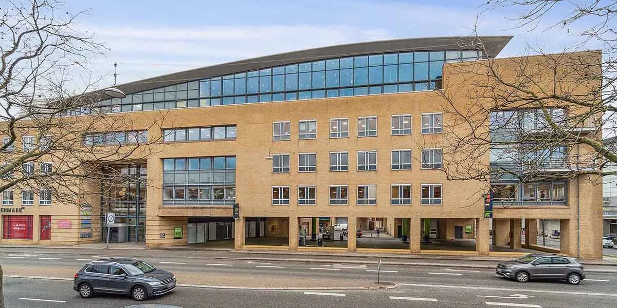 To biler kører på hovedgaden med bygning med glasfassade og garageindkørsel i forgrunden