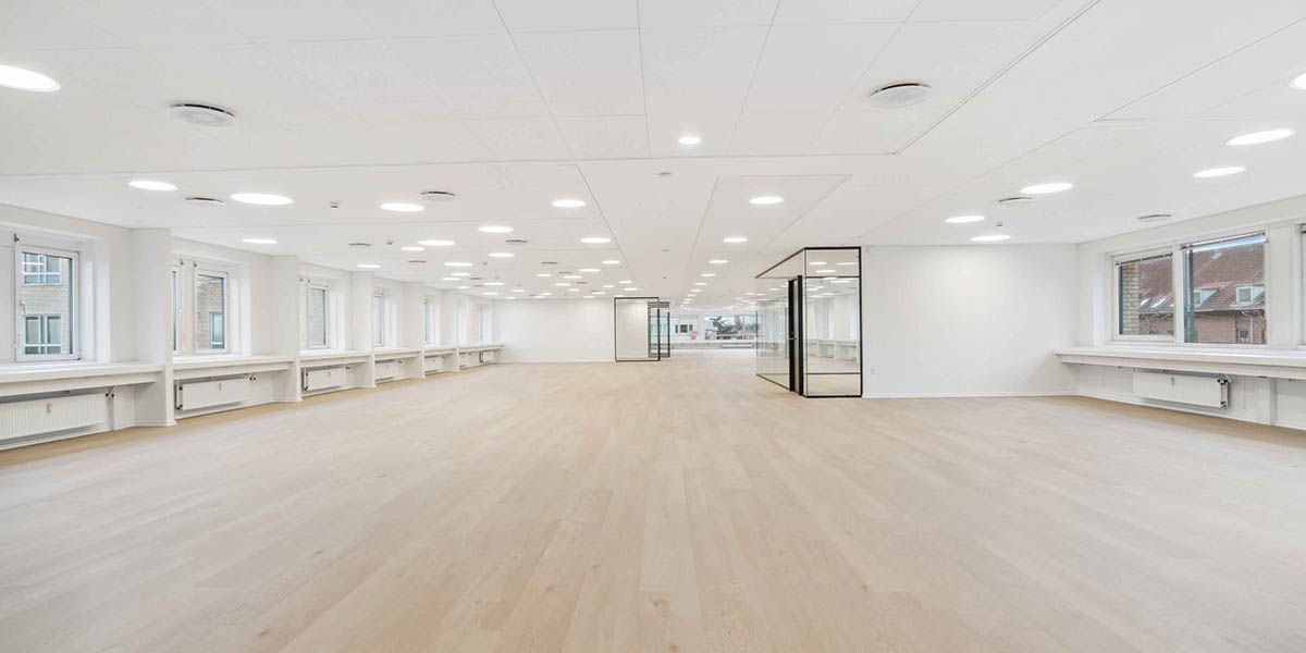 Ledig og præsentabel lejlighed med lyse gulve og store vinduer mod gaden, hvor der er et lille glasdækket område