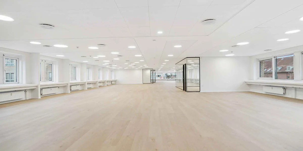 Ledig og præsentabel lejlighed med lyse gulve og store vinduer mod gaden, hvor der er et lille glasdækket område