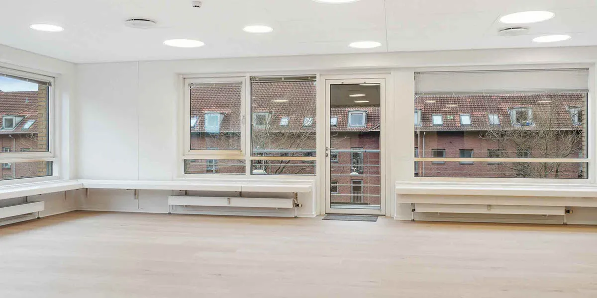 Lejlighed med fire vinduer, to døre og pære-lys på loftet i en stor, tom rum med lysegulve og hvide vægge