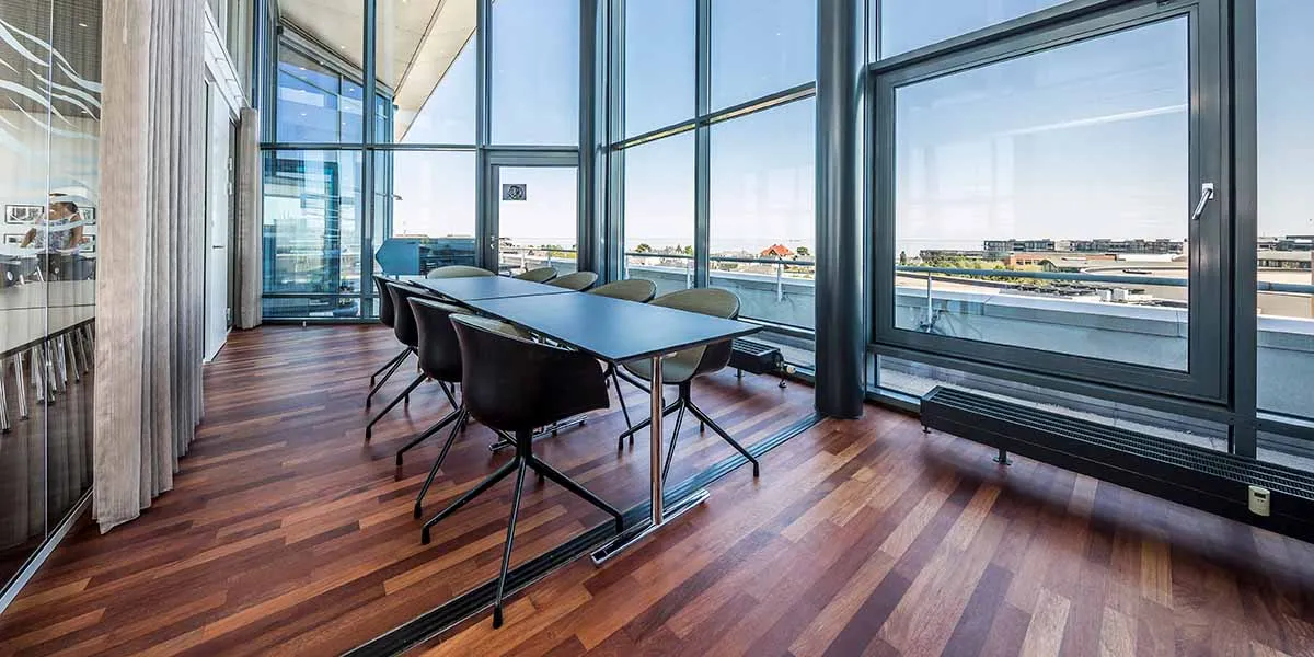 Et luksuriøst mødelokale med glasvinduer og udsigt over byen, hvor lyse og lyse stole står rundt om et langt bord med udsigt