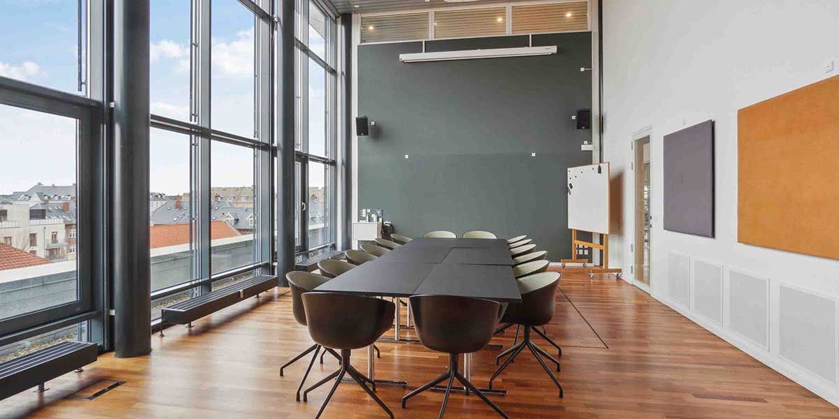 Mødelokalet er i lysebrunt og gråt med trægulve, høje ruder og lysegule vægge