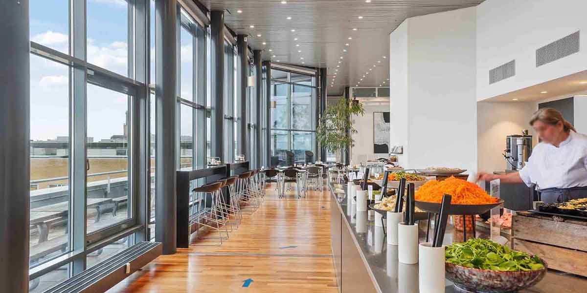 Buffetbord med rødbeder, salat, kartofler og grøntsager i restauranten med udsigt til byen fra glasvinduer og trægulv