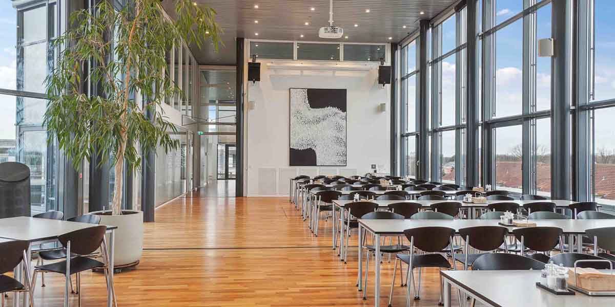 Indvendigt lukket restaurant med trægulve, glasvinduer og moderne møbler samt en stor indendørs plante