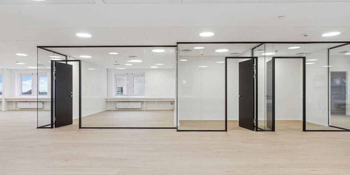 Ledig kontor med gulv, vægge og lofter i hvidt og glas samt fire glasdøre og vinduer med udsigt til byen og himlen