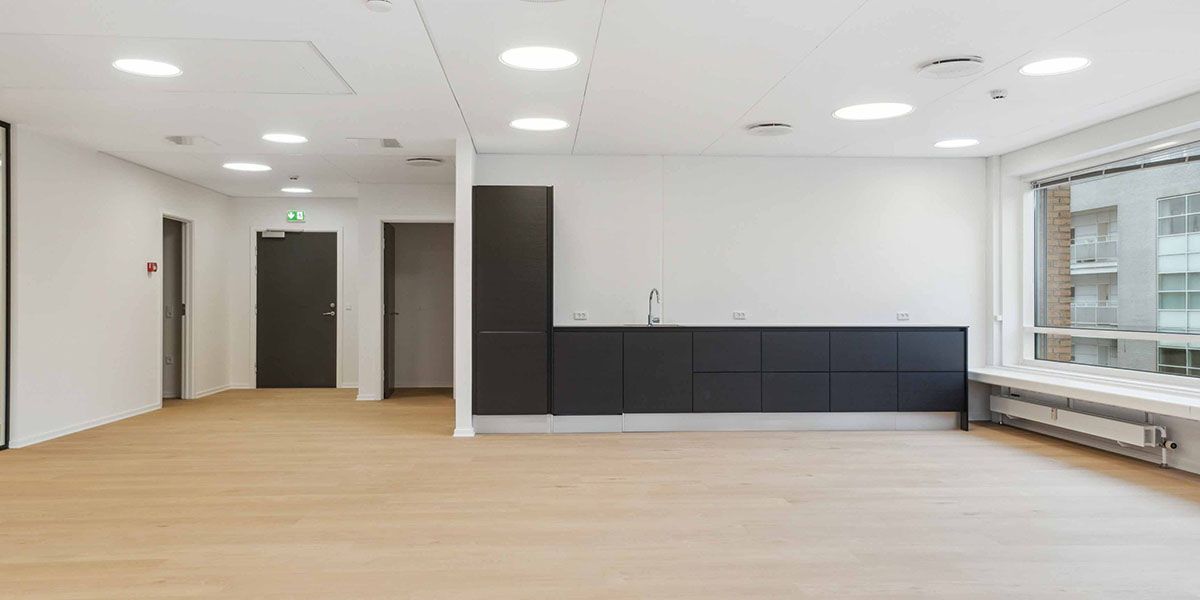 Lys og moderne kontorlokaler med åbne døre, højloft, lysepunkter, lysegul gulvbelægning, køkken med hængeskabe og vask samt