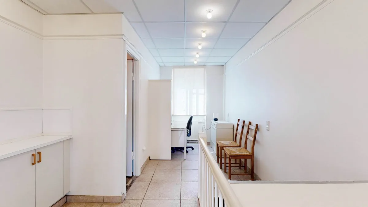 Indenfor er en lyse hall med en hvid væg og to træstole mod højre. Der er to skabe med gule håndtag til venstre. Der er fire