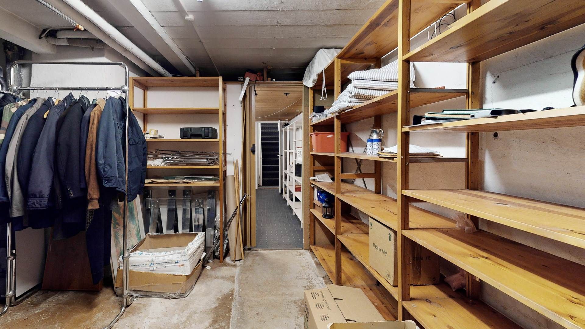 Tidligere lager med tøj, bøger, papkasser og diverse genstande i en lyse, rummelig rum.