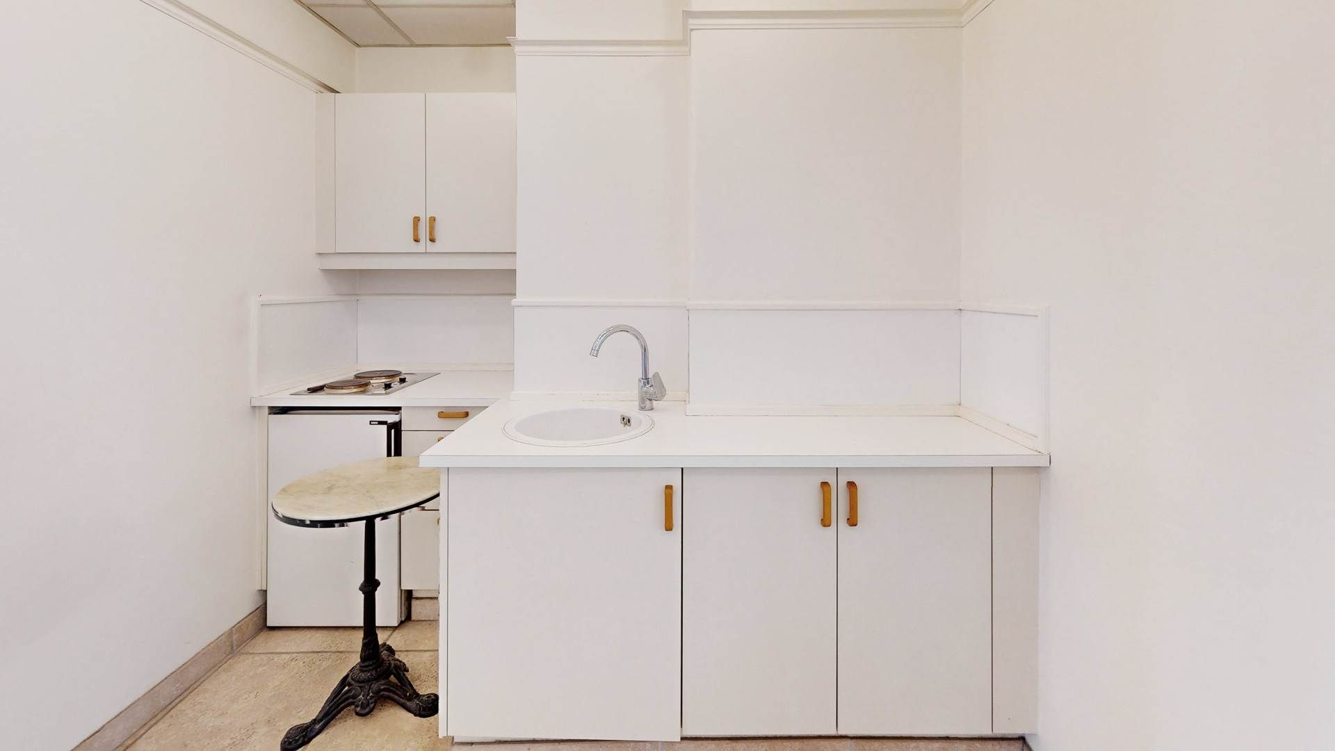 Et rent, minimalistisk køkken med en hvid væg og hvide skabe, en ren hvid vask og en høj marmor barbord