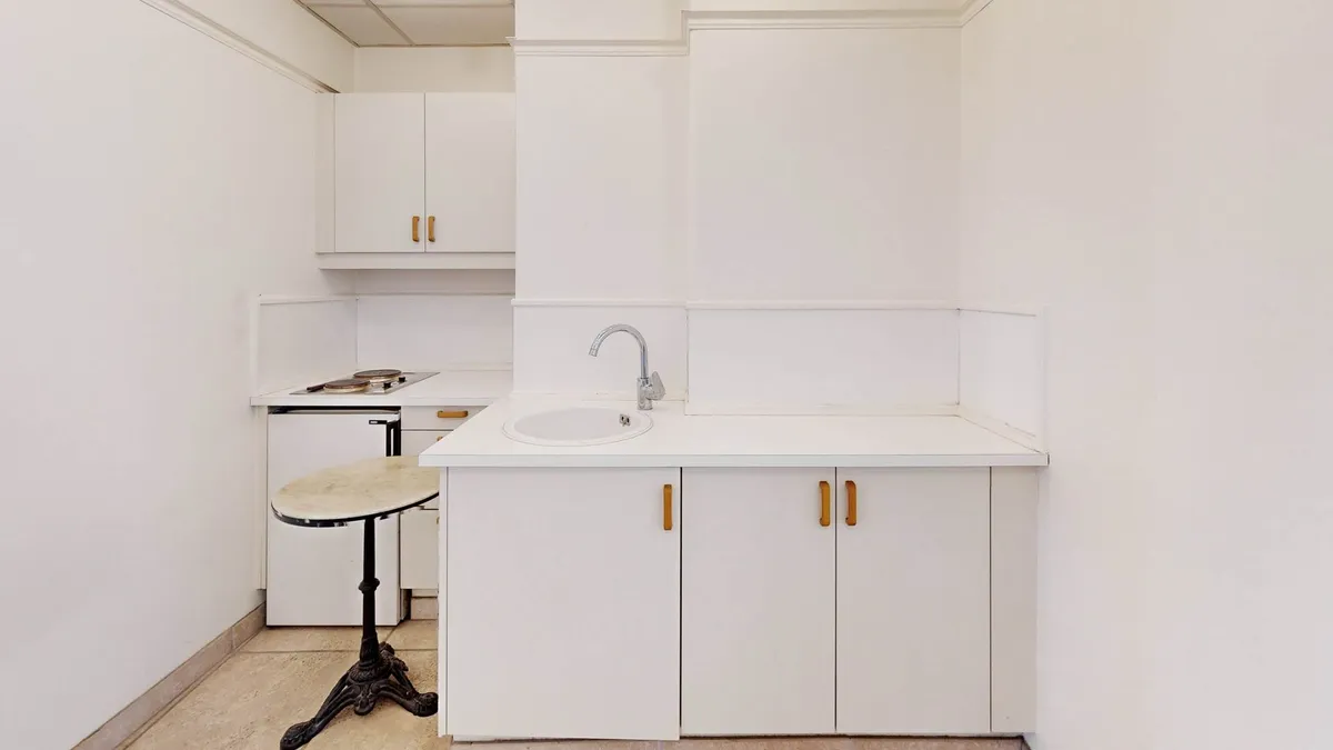 Et rent, minimalistisk køkken med en hvid væg og hvide skabe, en ren hvid vask og en høj marmor barbord