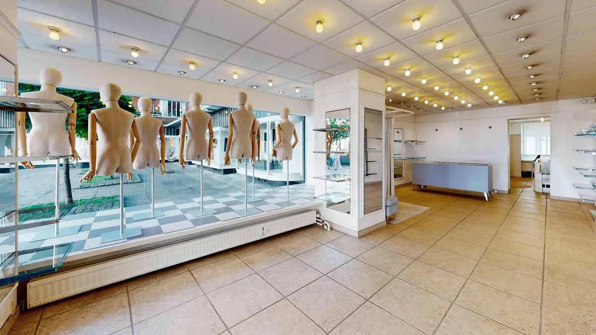 Inde i forretningen er der slanke mannedukker i linned og et gulv med lysegrå fliser samt et gult skur og hvidt loft
