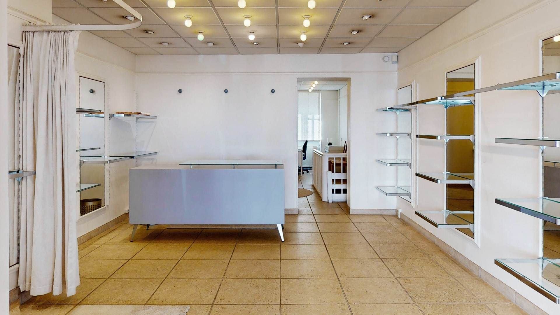 Smuk kontorlokaler med lysegult gulv og hvide vægge, glashylder og spejle samt en hvid stang med hvid gardin foran