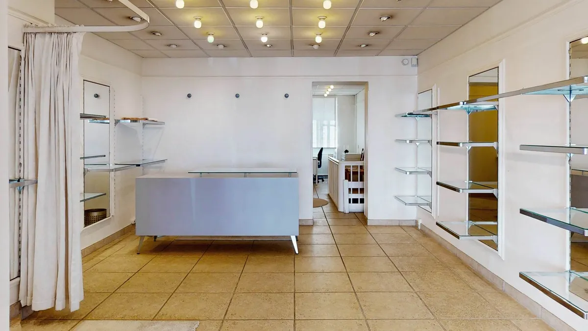 Smuk kontorlokaler med lysegult gulv og hvide vægge, glashylder og spejle samt en hvid stang med hvid gardin foran