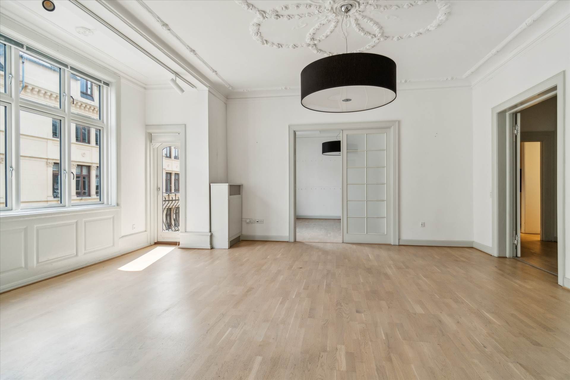 Torum med højt til loftet, hvidmalede vægge, lyse trægulve, to store glasvinduer og et hængelampe i sort og hvid.