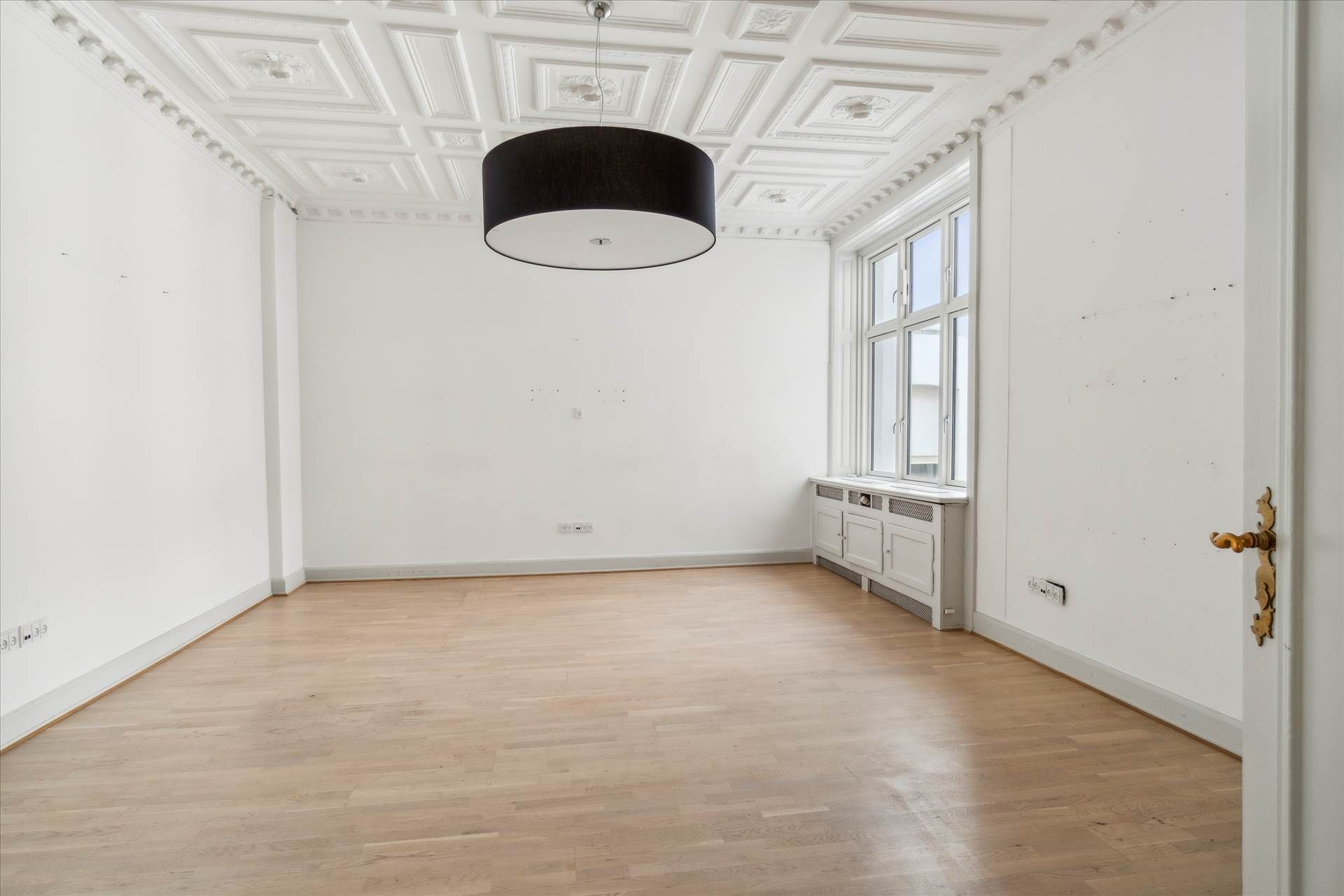 Elegant herskabeligt kontor med højloftede rum, blanke gulve og hvide vægge samt lyse vinduer og hængende loftslampe