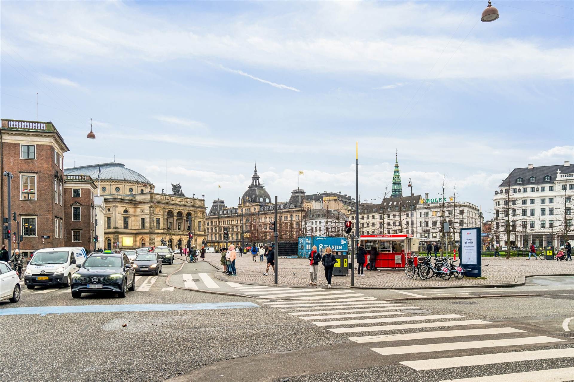 Mennesker går rundt i byen og kører biler i Bredgade i København. De fleste mennesker går på fodgængerfeltet, og der er både