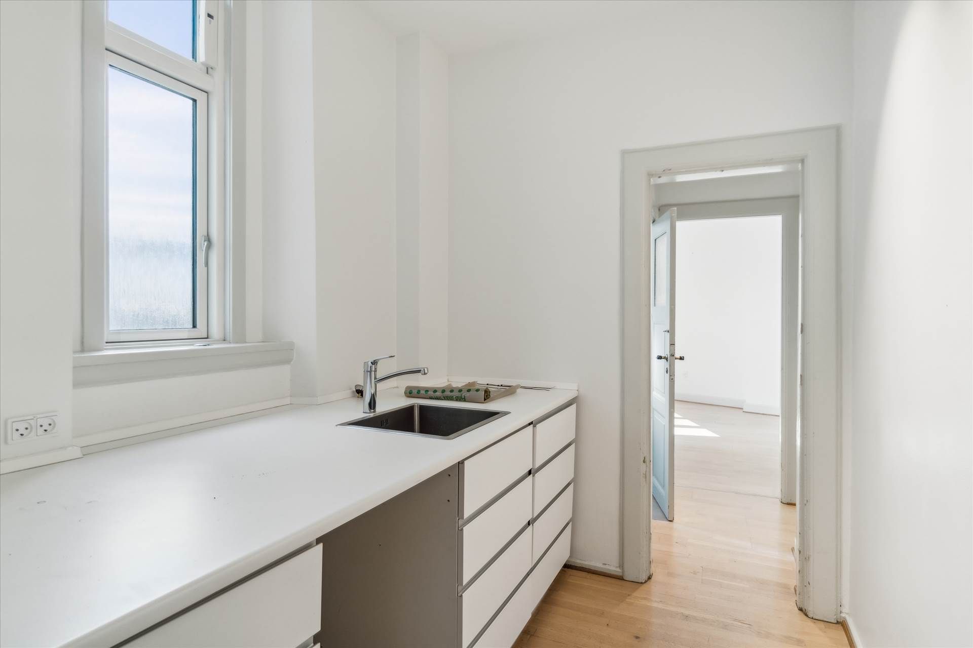 Hvidt badeværelse med køkkenblok, hvor der er en håndvask, skabe og loftsvinduer med udsigt til skyerne