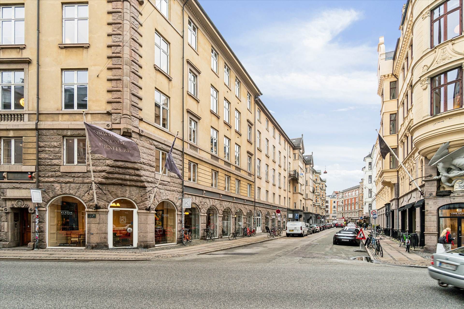 Københavnsgader med udsigt til en vej med biler og cykler og faglæste butikker med mærker og flag