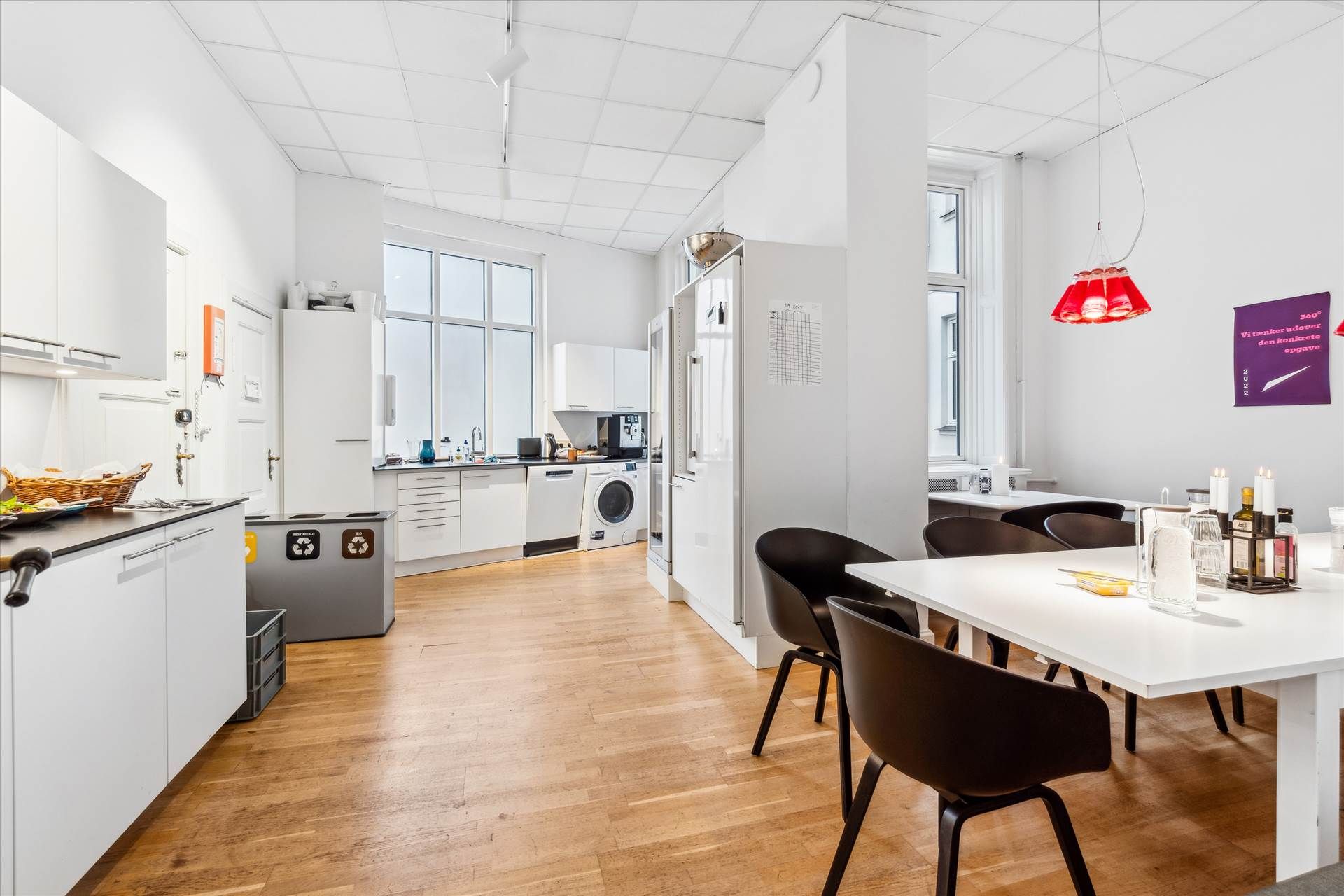 Lys moderne køkken med hvidt køkkeninventar, hvidt gulv og bord med to stole og lysekroner