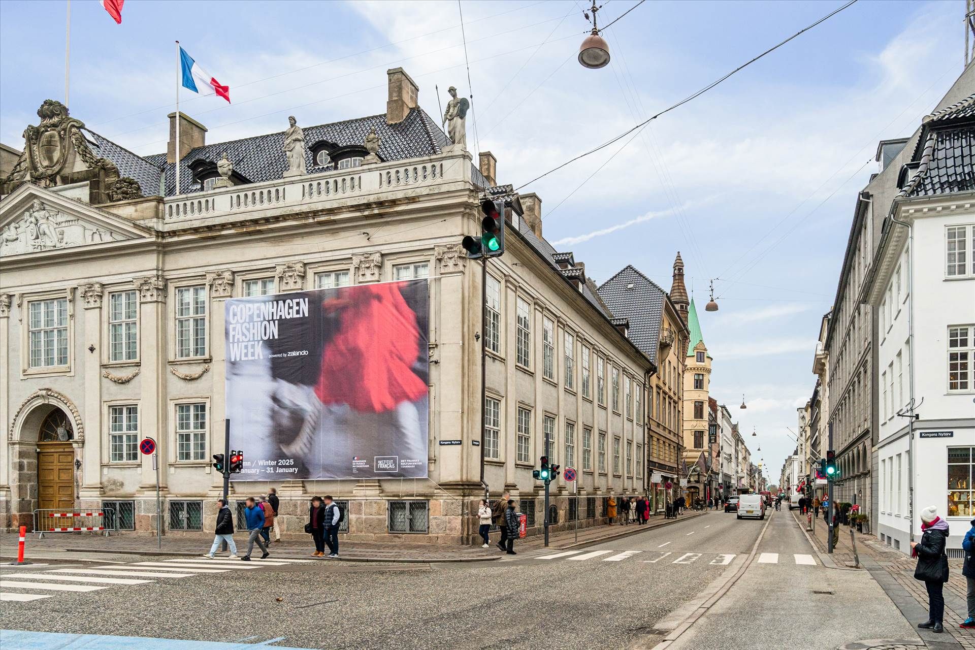 Mennesker går på gågaden foran et bygning med udsigt til Københavns gamle bydel. Et stort banner med teksten Copenhagen