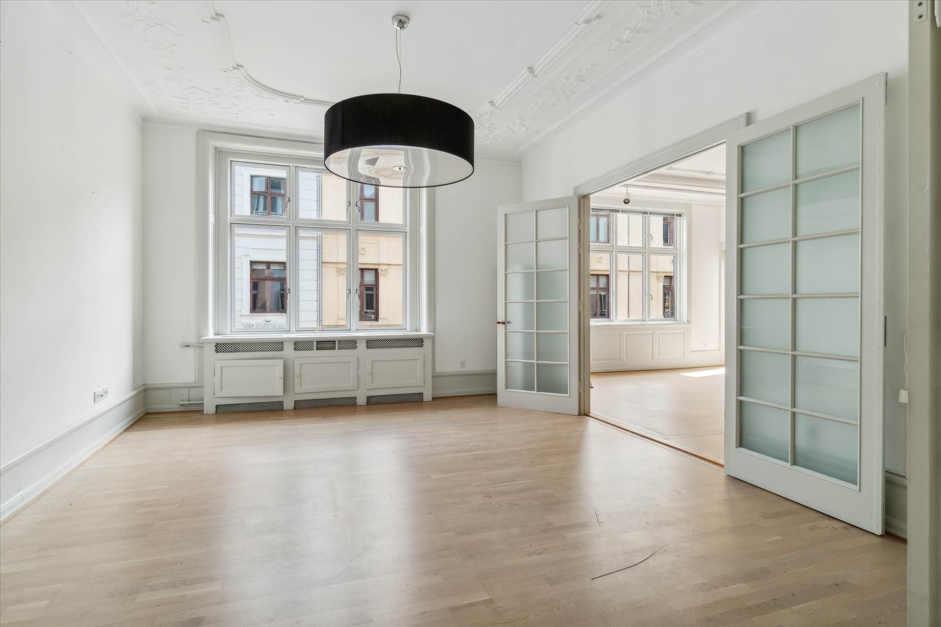 Herskabeligt kontor med åbne hvide døre og lyse gulvplanker og hvide vægge med lysekroner og vinduer med udsigt til bygning