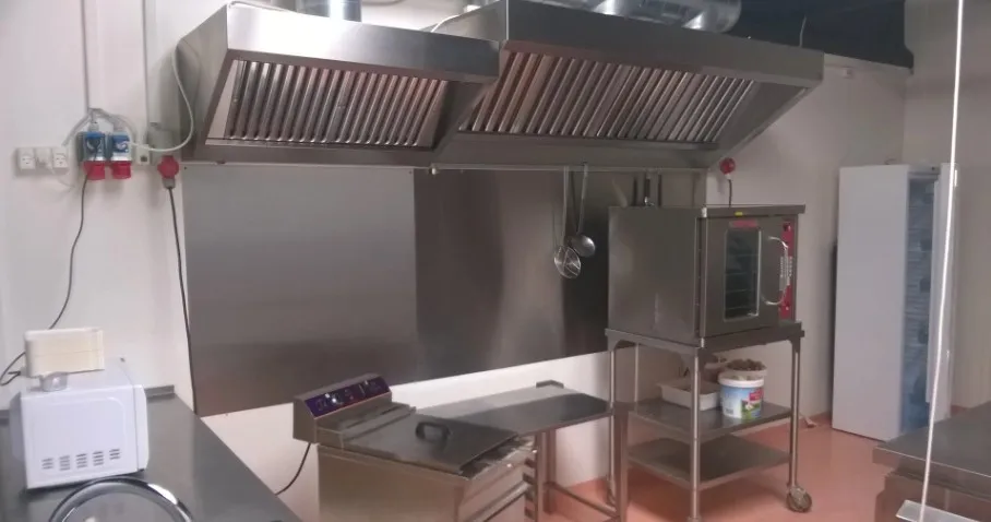 Professionelt indrettet kommerciel køkken med røgudsugning, induktionskomfur, ovn og køleskab samt flere hylder og