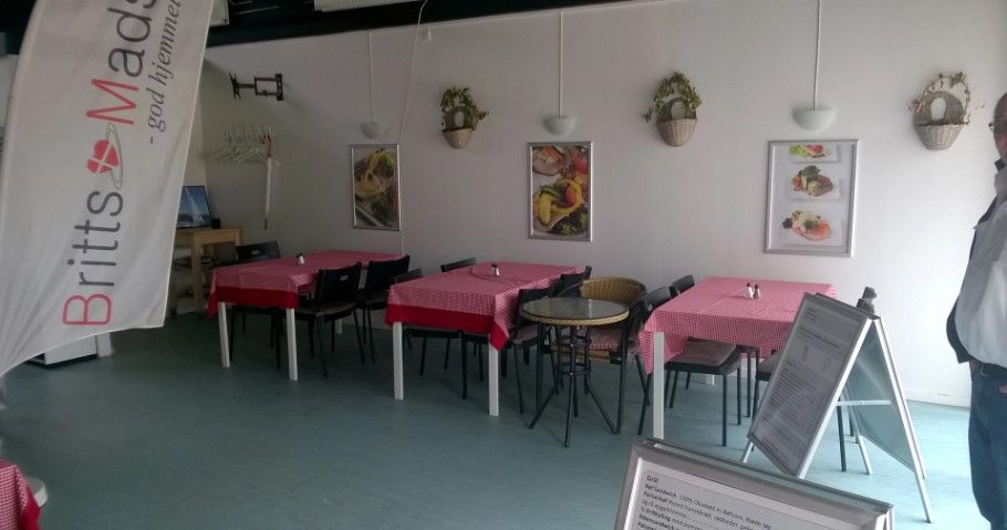 Tomme stole og borde i et spisested med rød-hvide servietter og plantepoter på væggen og en mand i en hvid skjorte og blå