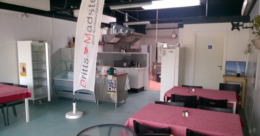 Indvendigt i en cateringvirksomhed er der en række røde og hvide borde med stole samt en flagpæl med reklame for britts