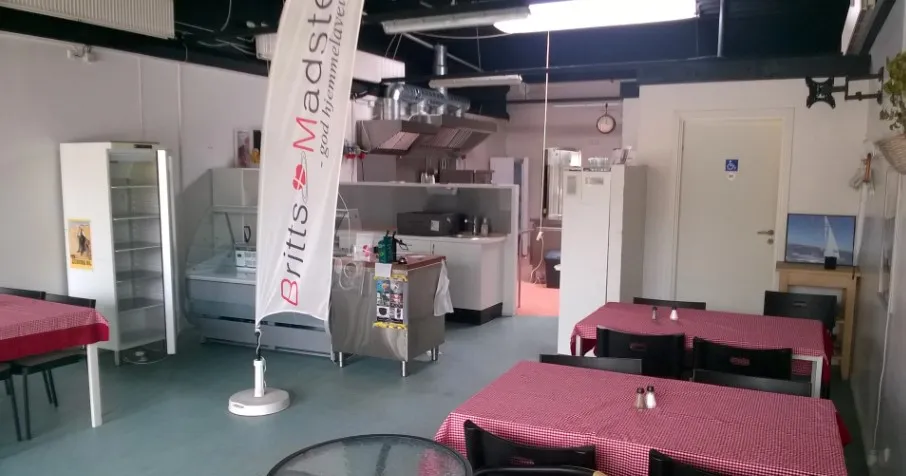 Indvendigt i en cateringvirksomhed er der en række røde og hvide borde med stole samt en flagpæl med reklame for britts