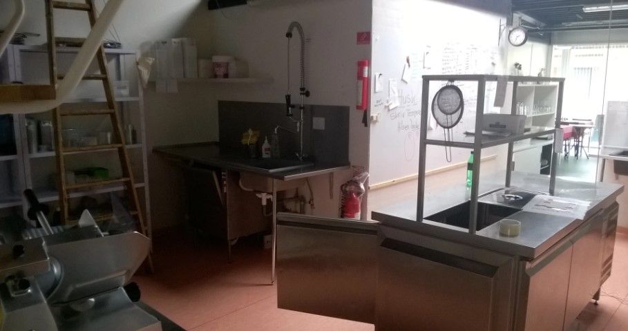 Køkken med rustfrit stålapparater, metalbord, åben dør, stiger, brændsleslukker, vægt, håndvask, og flere artikler på hylder