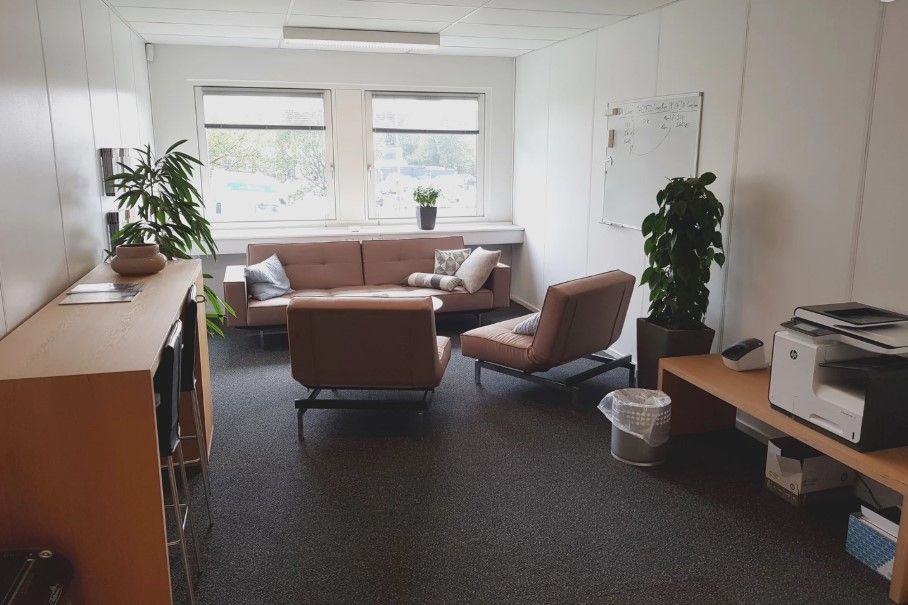 Kontorlokale med skrivebord, sofa, stol, plante, papkasser og en printer på en bord