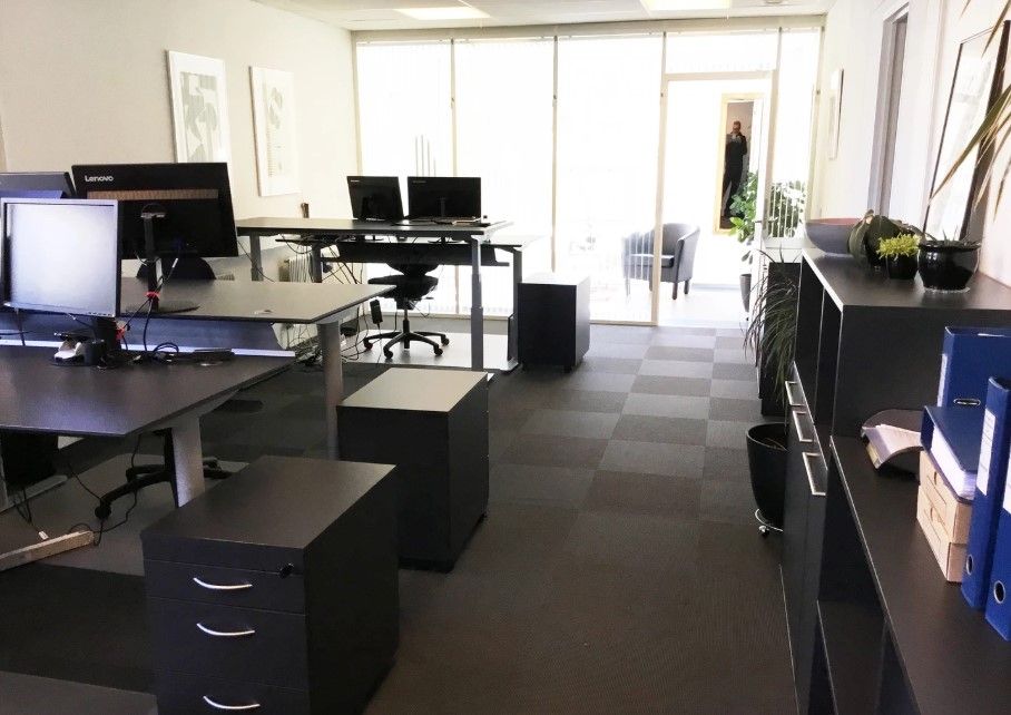 Kontorlokale med skriveborde, stole, skærme, blomster, plantepotter og flere møbler og udstyr