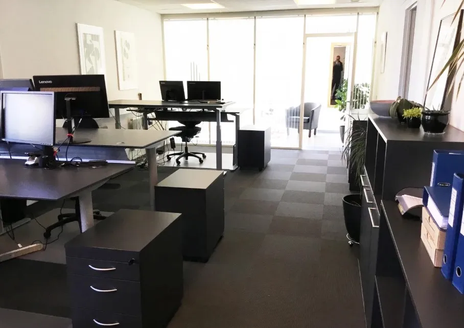 Kontorlokale med skriveborde, stole, skærme, blomster, plantepotter og flere møbler og udstyr