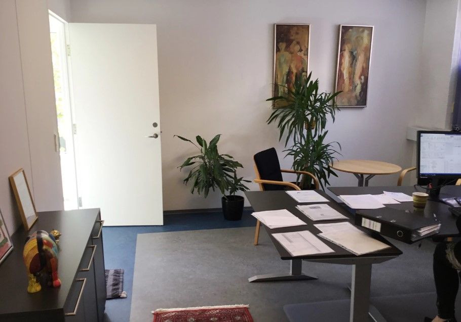 Kontorlokale med papegøjeplanter, en kaffekop, et computerskrivebord, flere papirer, en stol og et maleri