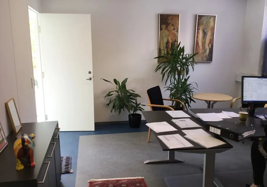 Kontorlokale med papegøjeplanter, en kaffekop, et computerskrivebord, flere papirer, en stol og et maleri