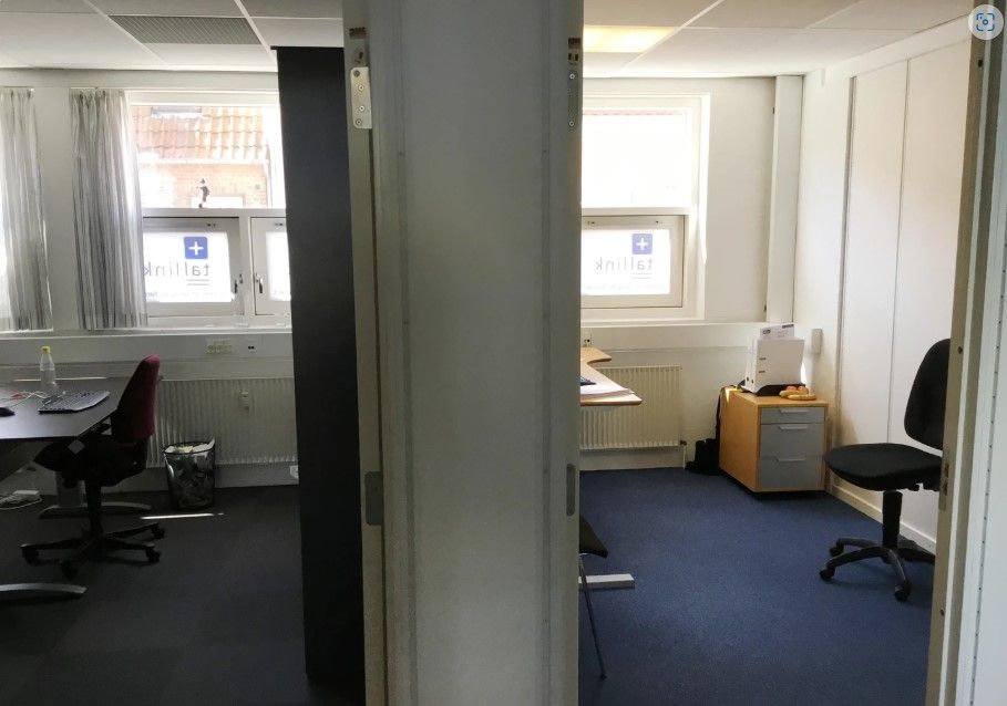 Kontorrum med skrivebord, stol og radiator samt et skraldspand og vandflaske.