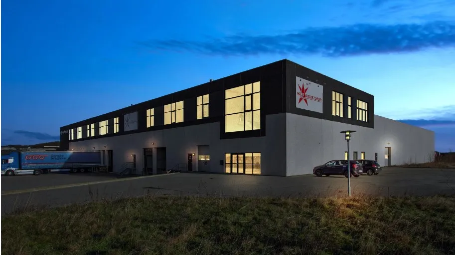 Rummeligt kontorlokale med fire vinduer, facade med rød stjerne og logo, biler parkeret og lastbil i baggrunden, lysene