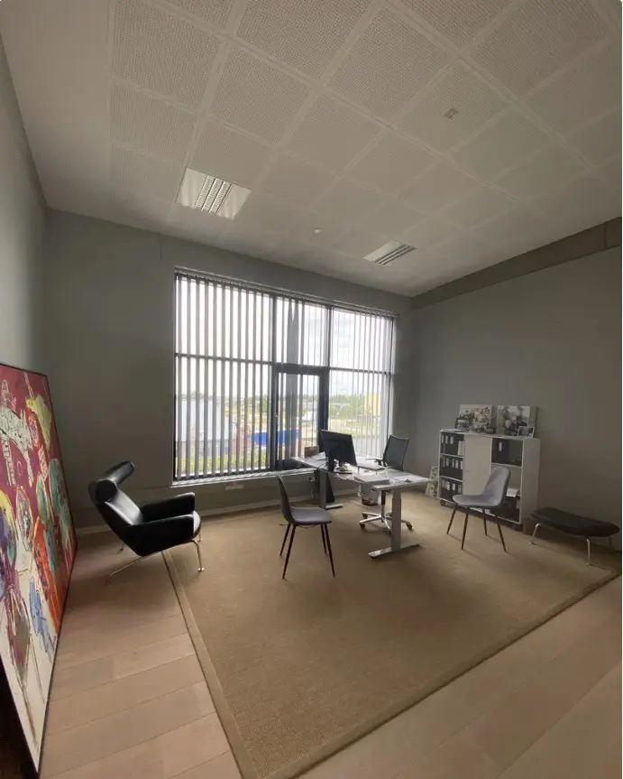 Kontorlokale med store vinduer, højt til loftet og trægulv. Moderne møbler og kunstværk udgør en elegant og professionel