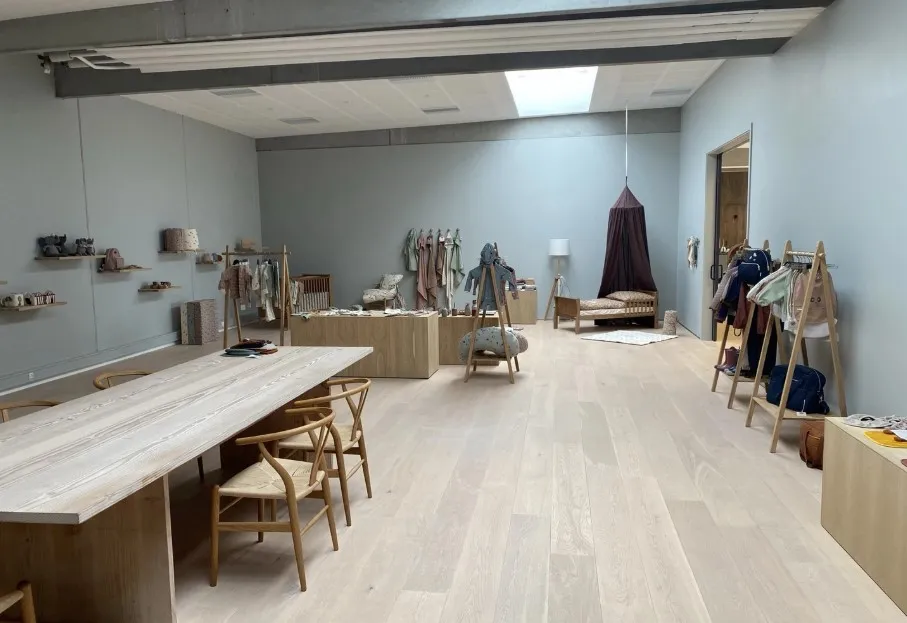 Rummeligt kontor med lyse trægulve og store vinduer, samt moderne møbler og en indretning med minimalistisk stil