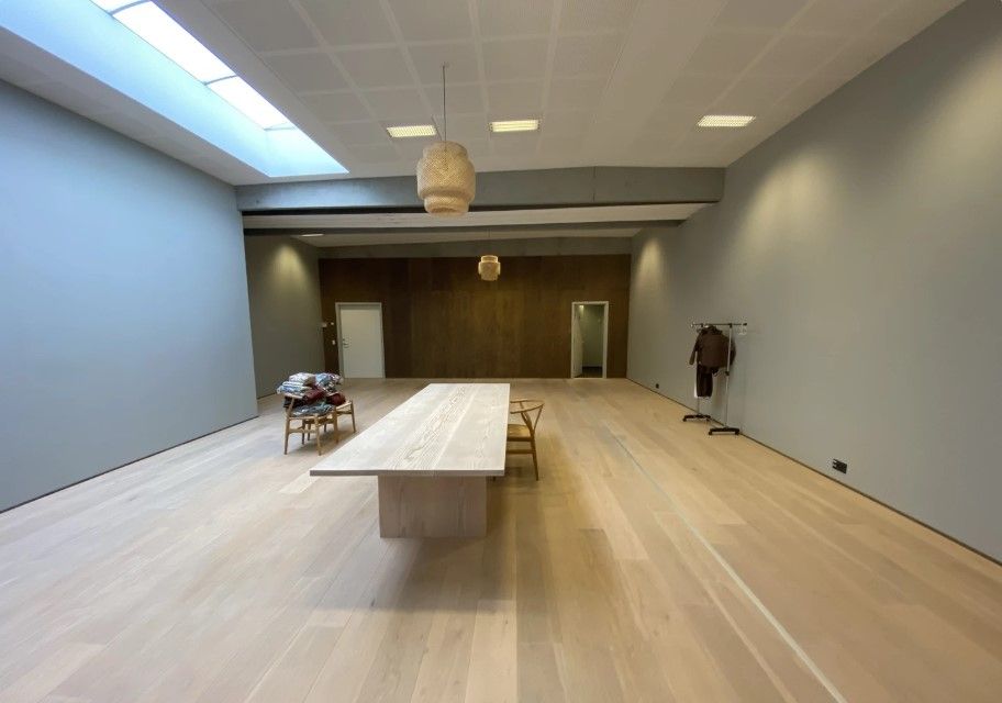 Et stort kontorlokale med lyse trægulve og hvide vægge og loft samt møbler og lysekroner i lysebrune nuancer